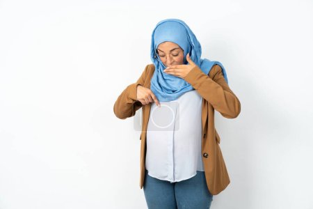 Foto de Impresionado hermosa mujer musulmana embarazada con hijab mirada sorprendida hacia abajo, indica en blanco con el dedo índice, Chica asustada - Imagen libre de derechos