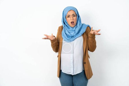 Photo for Frustrated beautiful pregnant muslim woman wearing hijab feels puzzled and hesitant, shrugs shoulders in bewilderment, keeps mouth widely opened, doesn't know what to do. - Royalty Free Image
