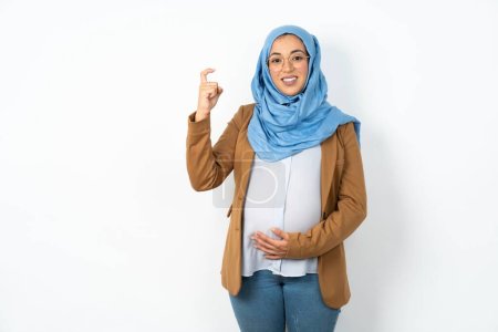 Foto de Mujer musulmana embarazada con hiyab apuntando hacia arriba con los dedos número nueve en lengua de signos china Jiu - Imagen libre de derechos