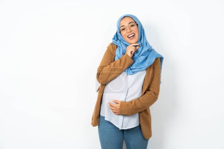 Photo for Beautiful pregnant muslim woman wearing hijab  laughs happily keeps hand on chin expresses positive emotions smiles broadly has carefree expression - Royalty Free Image