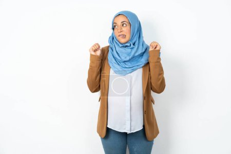 Téléchargez les photos : Belle femme musulmane enceinte portant hijab serre les poings et attend quelque chose de beau arrivé regarde loin mord les lèvres et attend l'annonce des résultats - en image libre de droit