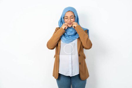 Photo for Pleased beautiful pregnant muslim woman wearing hijab  with closed eyes keeps hands near cheeks and smiles tenderly imagines something very pleasant - Royalty Free Image
