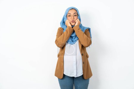 Photo for Beautiful pregnant muslim woman wearing hijab with surprised expression keeps hands under chin keeps lips folded makes funny grimace - Royalty Free Image