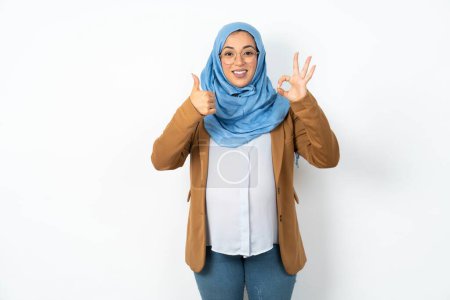 Foto de Hermosa mujer musulmana embarazada vistiendo hijab sonriendo y mirando feliz, despreocupada y positiva, haciendo un gesto de victoria o paz con una mano - Imagen libre de derechos