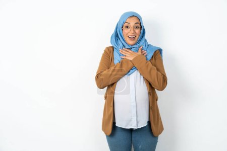 Photo for Beautiful pregnant muslim woman wearing hijab expresses happiness, laughs pleasantly, keeps hands on heart - Royalty Free Image