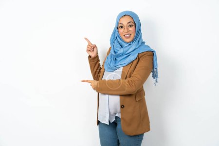Téléchargez les photos : Belle femme musulmane enceinte portant des points hijab à l'espace de copie indique pour la publicité donne la bonne direction - en image libre de droit
