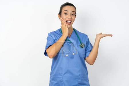 Téléchargez les photos : Fou arabe médecin femme portant uniforme bleu conseillant des prix discount tenir la paume ouverte nouveau produit - en image libre de droit