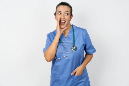 Foto de Árabe médico mujer vistiendo azul uniforme escuchar increíble privado noticias impresionado grito compartir - Imagen libre de derechos