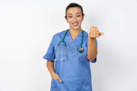 Foto de Médico árabe mujer con uniforme azul invitando a venir con la mano. Feliz de que hayas venido. - Imagen libre de derechos