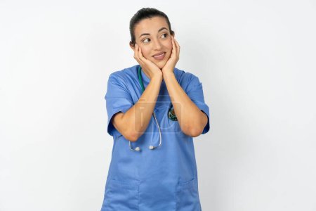 Téléchargez les photos : Inspiré arabe médecin femme portant uniforme bleu regardant copyspace ayant des pensées sur les événements futurs - en image libre de droit