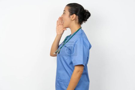 Photo for Half-faced close up portrait of astonished amazed arab doctor woman wearing blue uniform  holding hand near mouth - Royalty Free Image
