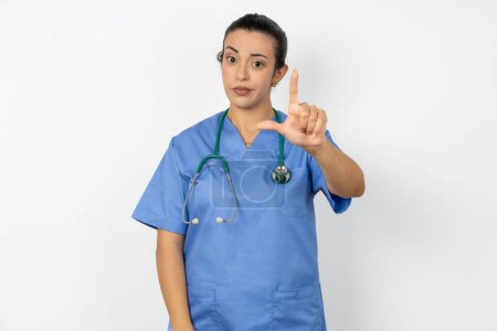 Photo for Arab doctor woman wearing blue uniform making fun of people with fingers on forehead doing loser gesture mocking and insulting. - Royalty Free Image