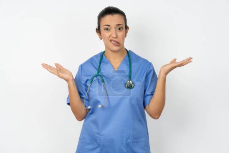Téléchargez les photos : Indignée médecin arabe femme portant des gestes uniformes bleus dans la confusion, fronce les sourcils face à l'insatisfaction. - en image libre de droit