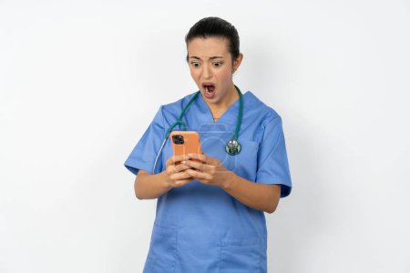 Téléchargez les photos : Focusedarab médecin femme portant uniforme bleu utilisation smartphone lecture nouvelles des médias sociaux, ou e-mail important - en image libre de droit