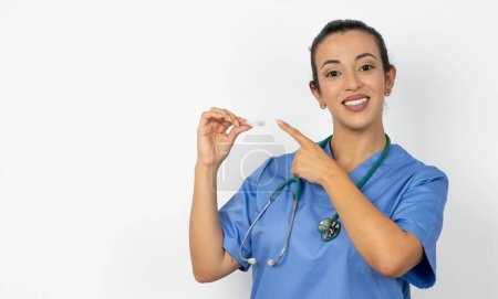 Téléchargez les photos : Femme arabe médecin en uniforme avec stéthoscope tenant un aligneur invisible et pointant vers elle. Concept de soins dentaires et de confiance. - en image libre de droit