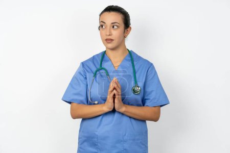 Téléchargez les photos : Femme arabe médecin en uniforme avec stéthoscope doigts raides et semble mystérieux de côté a un grand plan maléfique à l'esprit - en image libre de droit