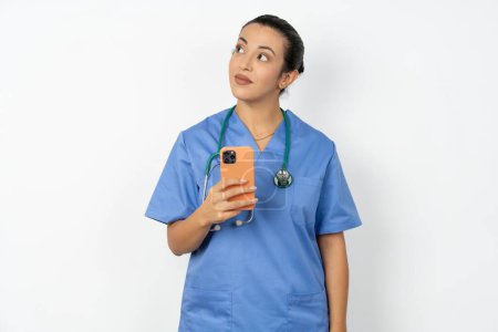 Foto de Mujer árabe médico vistiendo uniforme azul sostiene teléfono móvil utiliza Internet de alta velocidad y las redes sociales tiene comunicación en línea. Concepto de tecnologías modernas - Imagen libre de derechos
