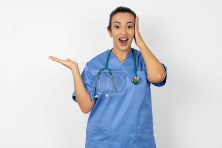 Foto de Sorprendido sorprendido sorprendido árabe médico mujer vistiendo azul uniforme agarre mano ofreciendo proposición - Imagen libre de derechos
