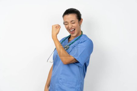 Foto de Retrato de la divertida mujer árabe médico con uniforme azul grito sí levantar los puños manos celebrar la competencia juego de la victoria - Imagen libre de derechos