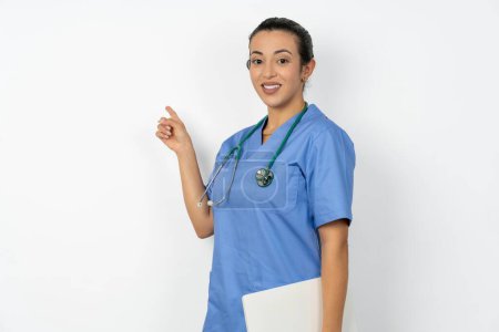 Foto de Árabe médico mujer vistiendo azul uniforme celebración portátil mostrando copia espacio vacío anuncio - Imagen libre de derechos