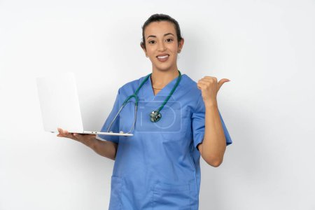 Photo for Arab doctor woman wearing blue uniform directing empty space  hold laptop - Royalty Free Image