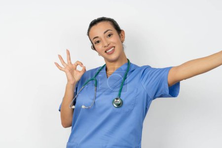 Foto de Retrato de bastante árabe médico mujer vistiendo uniforme azul hacer selfie show okey símbolo - Imagen libre de derechos