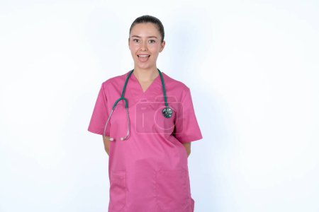 Foto de Médico mujer caucásica en uniforme rosa con estetoscopio con la cara feliz y divertida sonriendo y mostrando la lengua. - Imagen libre de derechos
