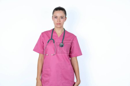 Foto de Mujer caucásica médico en uniforme rosa con estetoscopio frunciendo el ceño sus cejas siendo disgustado con algo. - Imagen libre de derechos