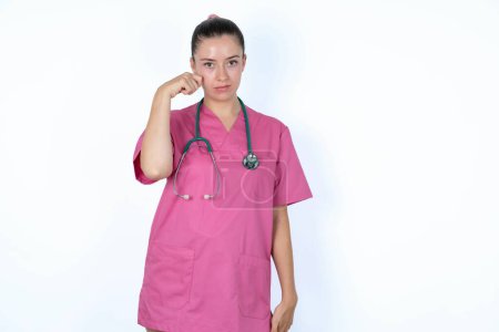 Photo for Unhappy caucasian woman doctor in pink uniform with stethoscope crying while posing at camera whipping tears with hand. - Royalty Free Image