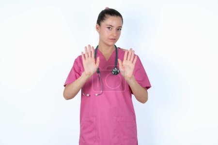 Photo for Caucasian woman doctor in pink uniform with stethoscope doing stop sing with palm of the hand. Warning expression with negative and serious gesture on the face. - Royalty Free Image