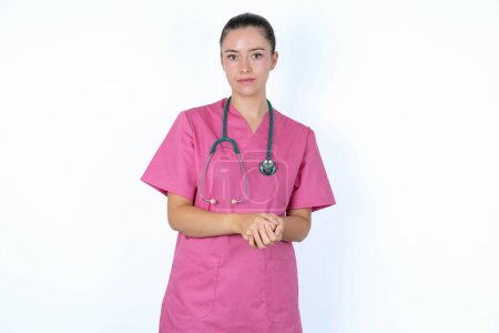 Téléchargez les photos : Concept d'affaires - Portrait de femme médecin caucasienne en uniforme rose avec stéthoscope tenant la main avec un visage confiant. - en image libre de droit