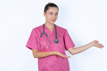 Photo for Portrait of caucasian woman doctor in pink uniform with stethoscope  with arms out in a welcoming gesture. - Royalty Free Image