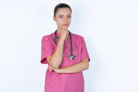 Photo for Caucasian female doctor with hand under chin and looking sideways with doubtful and skeptical expression, suspect and doubt. - Royalty Free Image