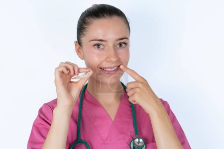Photo for Caucasian female doctor holding an invisible aligner and pointing to her perfect straight teeth. Dental healthcare and confidence concept. - Royalty Free Image