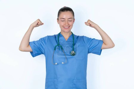 Photo for Strong powerful caucasian female doctor toothy smile, raises arms and shows biceps. Look at my muscles! - Royalty Free Image