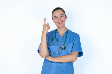 Téléchargez les photos : Médecin femme caucasienne souriant et regardant amical, montrant numéro un ou premier avec la main vers l'avant, compte à rebours - en image libre de droit