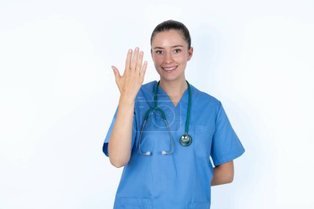 Foto de Médico femenino caucásico sonriendo y mirando amistoso, mostrando el número cinco o quinto con la mano hacia adelante, cuenta atrás - Imagen libre de derechos