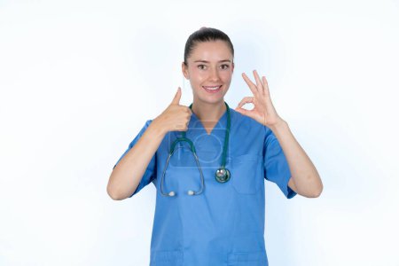 Téléchargez les photos : Femme caucasienne médecin souriant et regardant heureux, insouciant et positif, geste de victoire ou de paix avec une main - en image libre de droit