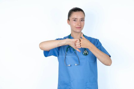 Téléchargez les photos : Femme caucasienne médecin en uniforme avec stéthoscope montrant pouce haut et bas signe - en image libre de droit