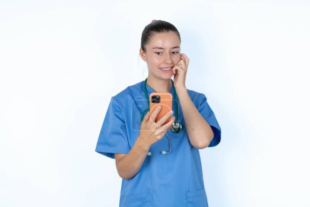 Foto de Mujer caucásica asustada médico en uniforme con estetoscopio sosteniendo teléfono y morder las uñas - Imagen libre de derechos