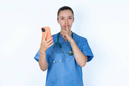 Foto de Caucásica mujer médico en uniforme con estetoscopio celebración moderno gadget pedir no contar secretos - Imagen libre de derechos