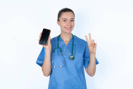 Photo for Caucasian woman doctor in  uniform with stethoscope holding modern device showing v-sign - Royalty Free Image