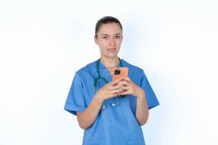 Foto de Foto de mujer caucásica médico en uniforme con estetoscopio mantenga el concepto de retroalimentación de desagrado de teléfonos inteligentes - Imagen libre de derechos