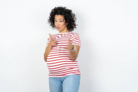 Foto de Mujer embarazada alegre guiño y señala los dedos índice a la cámara, elige a alguien, hace pistola de dedo. - Imagen libre de derechos