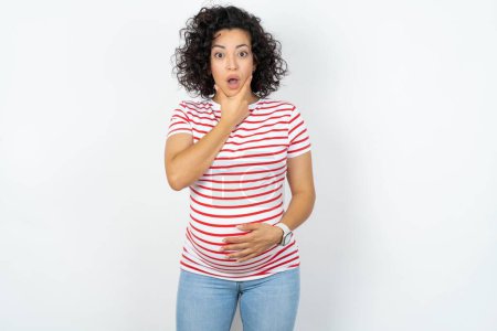 Foto de Mujer embarazada Mirando fascinado con incredulidad, sorpresa y expresión asombrada con las manos en la barbilla - Imagen libre de derechos