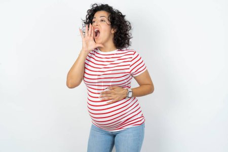 Foto de Mujer embarazada gritando y gritando fuerte a un lado con la mano en la boca. Concepto de comunicación. - Imagen libre de derechos
