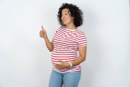 Téléchargez les photos : Femme enceinte L'air fier, souriant faire les pouces vers le haut geste sur le côté. Bon travail.! - en image libre de droit