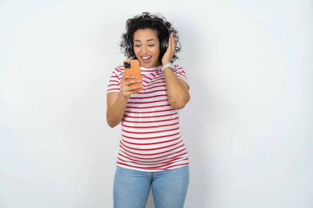 Foto de Mujer embarazada feliz se siente bien mientras se centra en la pantalla del teléfono inteligente. - Imagen libre de derechos