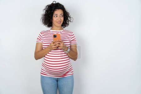 Téléchargez les photos : Femme enceinte tenir téléphone mains lire de bonnes nouvelles de la jeunesse regarder espace vide annonce - en image libre de droit