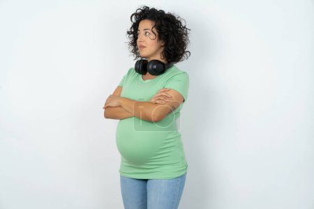 Téléchargez les photos : Femme enceinte agréable garde les mains croisées sur la poitrine semble heureusement de côté - en image libre de droit